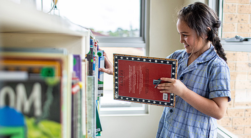 Student pulling book off shelf at Our Lady of the Rosary Catholic Primary School St Marys
